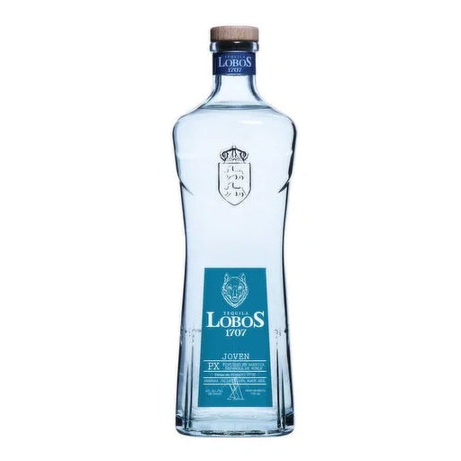 A bottle of Lobos 1707 Joven Tequila, co-founded by LeBron James, stands on a rustic wooden surface. The clear bottle showcases the tequila's light color, a result of its unique blend and finishing in sherry barrels using the Solera method.